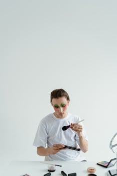 Young man using makeup brushes and eyeshadow palette on a white background.