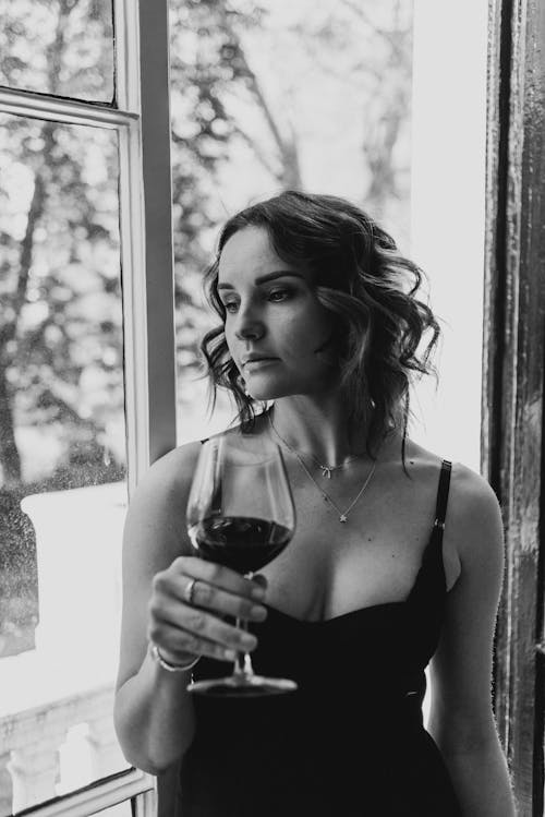 Free Thoughtful woman with glass of wine near window Stock Photo