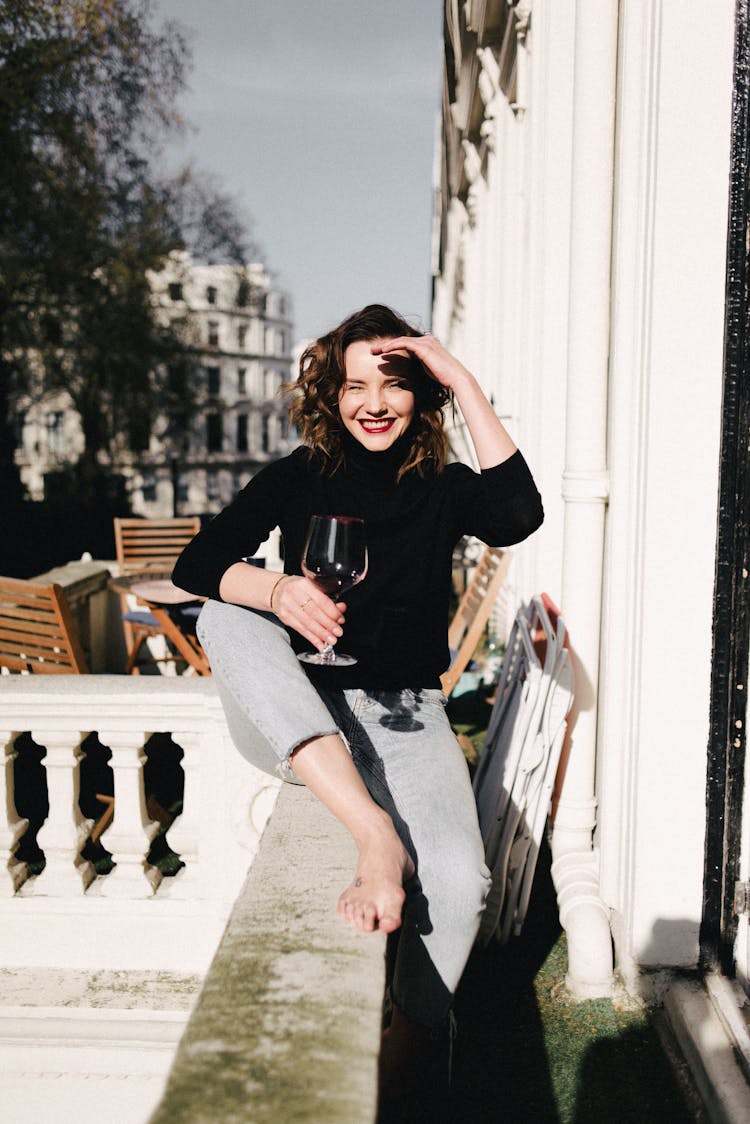 Smiling Woman With Red Wine On Balcony Fence