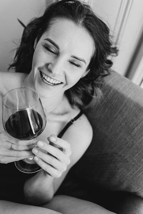 Cheerful woman with glass of wine in armchair at home