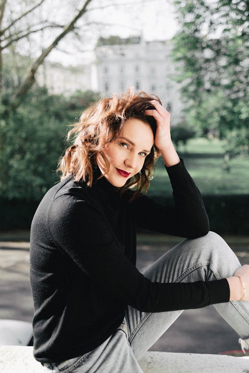 Smiling woman touching hair on fence against park