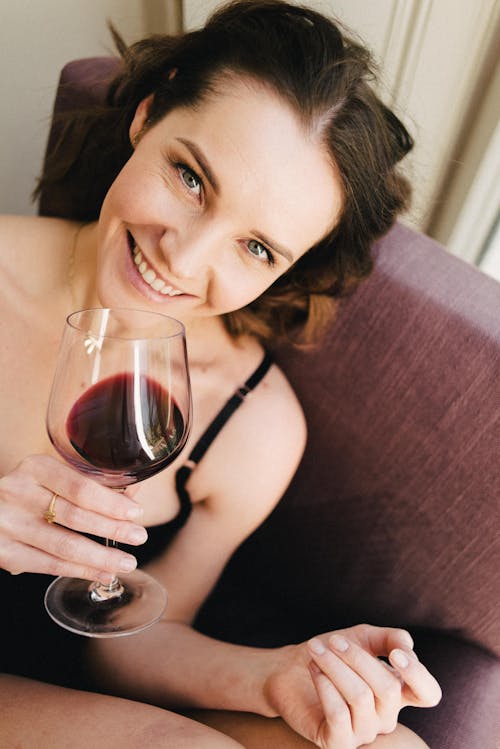 Free Smiling woman with red wine in armchair at home Stock Photo