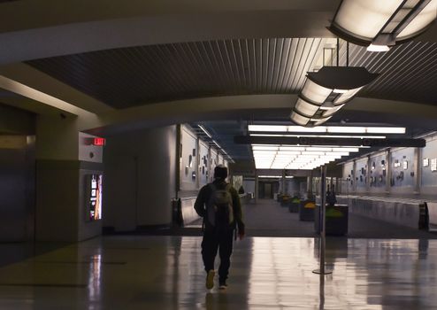 Silhouette of a man walking through a modern and dimly lit airport terminal at night.