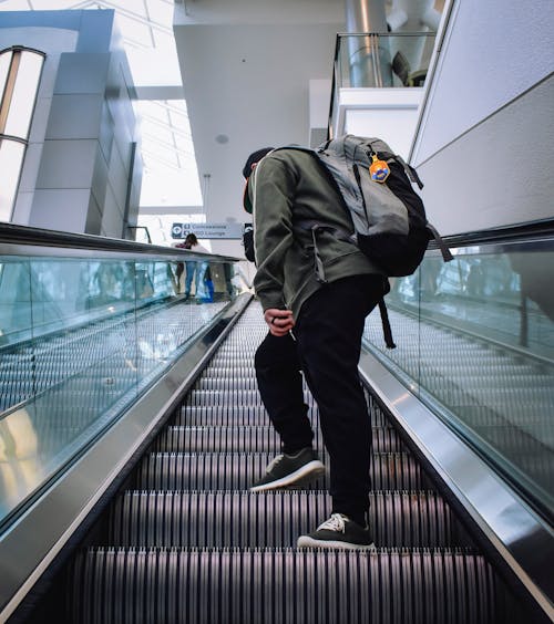 Man in Black Pants with Backpack Standing on the Escalator