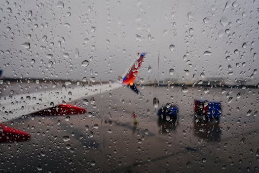 Raindrops on a window with an airplane in the background at an airport, creating a moody travel scene.