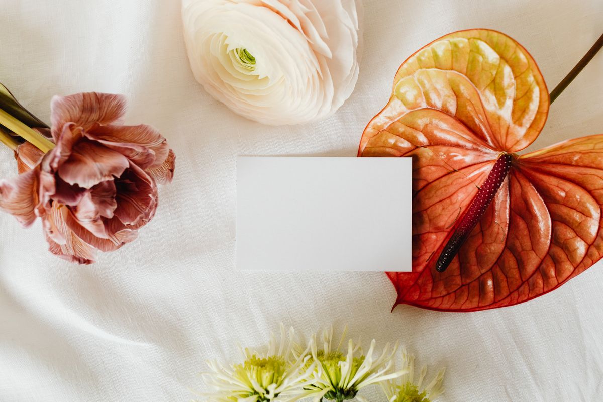 Tấm thiệp trắng để trống giữa hoa mao lương, tulip, hồng môn trên nền vải trắng