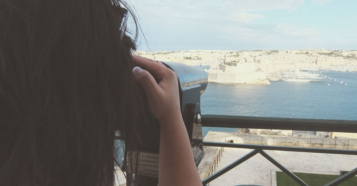 A woman enjoys a scenic view of the harbor using binoculars from a viewing platform.