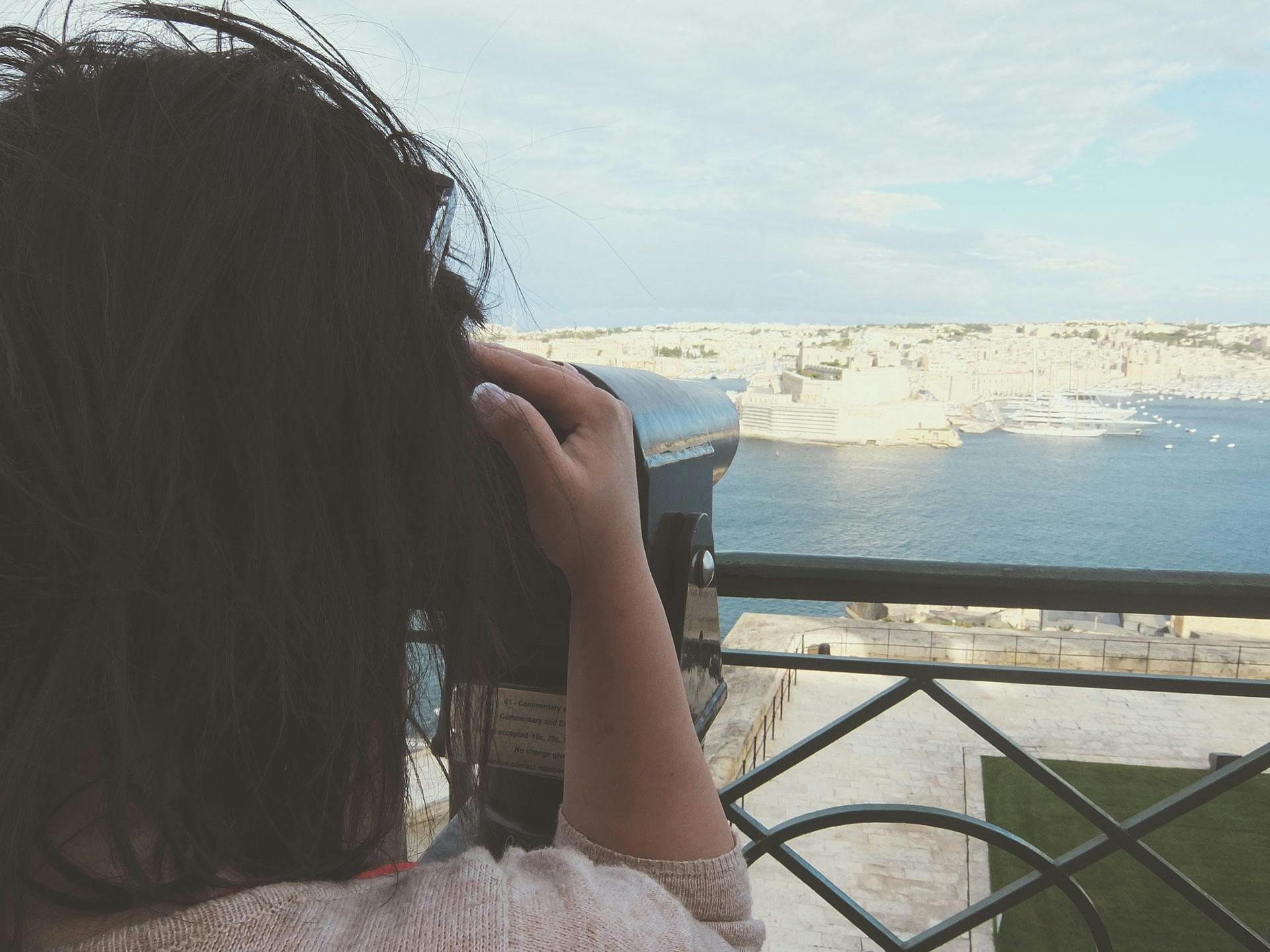 A woman enjoys a scenic view of the harbor using binoculars from a viewing platform.