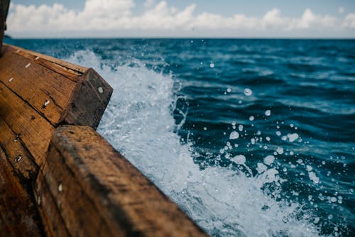 Detail of shabby wooden boat sailing in blue sea and splashing water in summer