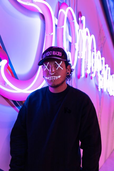 A person wearing a neon mask stands against vibrant neon lights in urban New York City at night.