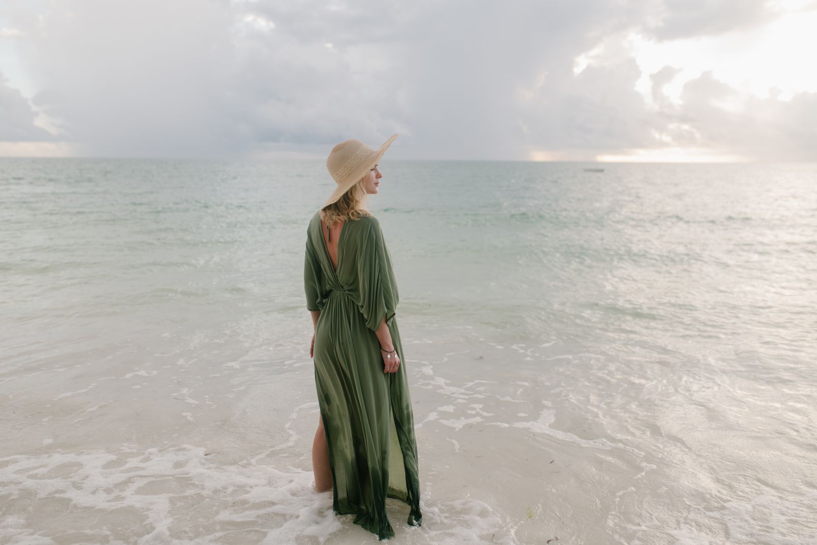 Woman wearing a flowing maxi dress and straw hat on a tropical beach