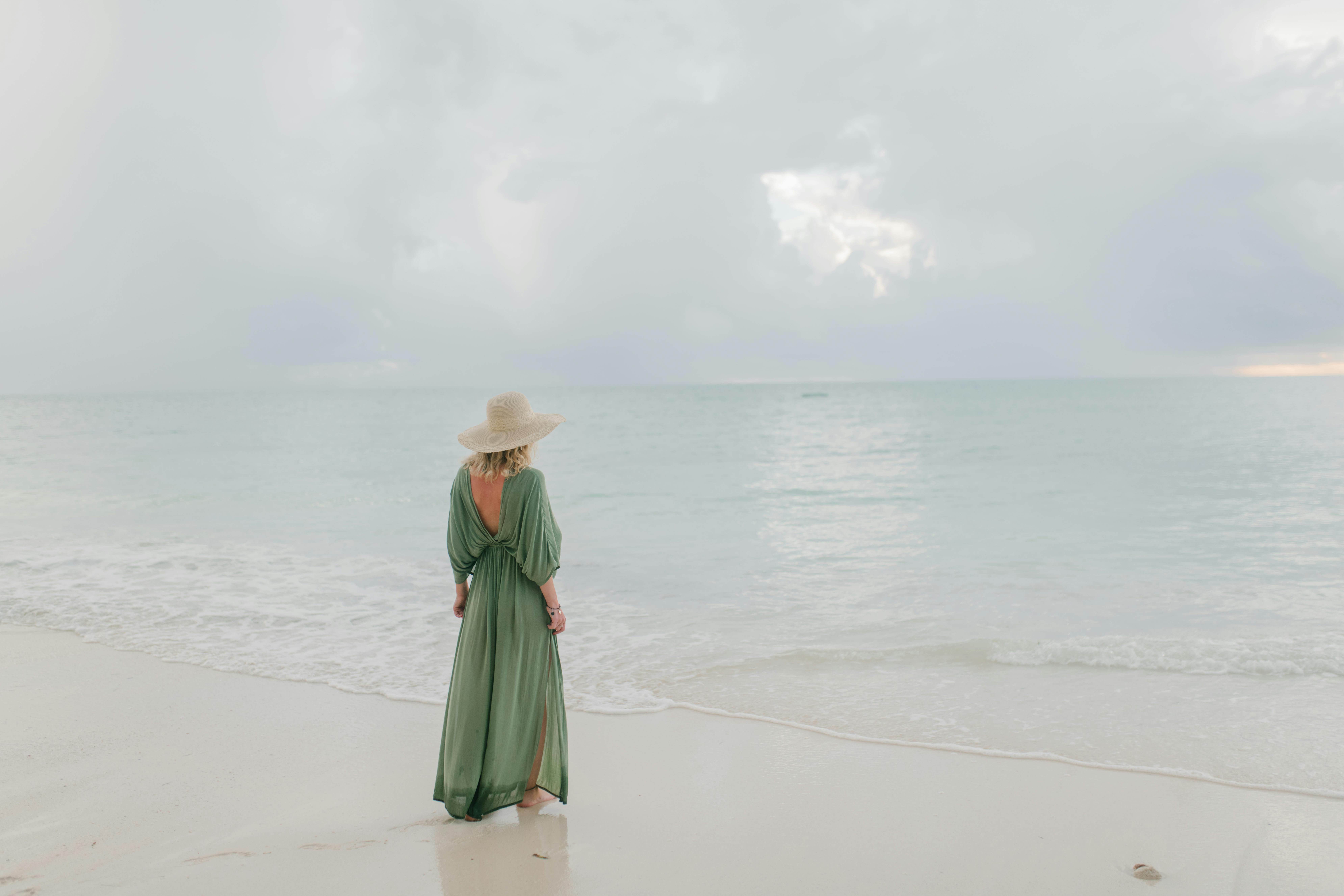 Full body back view of unrecognizable female tourist standing on sandy beach and admiring endless clear sea