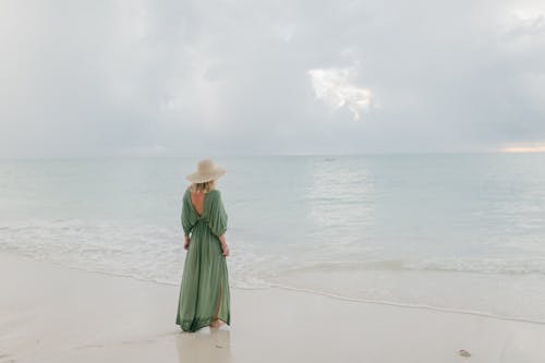 Woman in dress and hat admiring seascape under cloudy sky