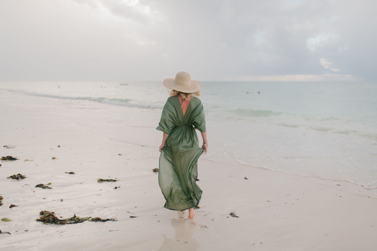 A woman in a flowing kaftan walking along a windy beach, why the kaftan is summer's most elegant throw-on