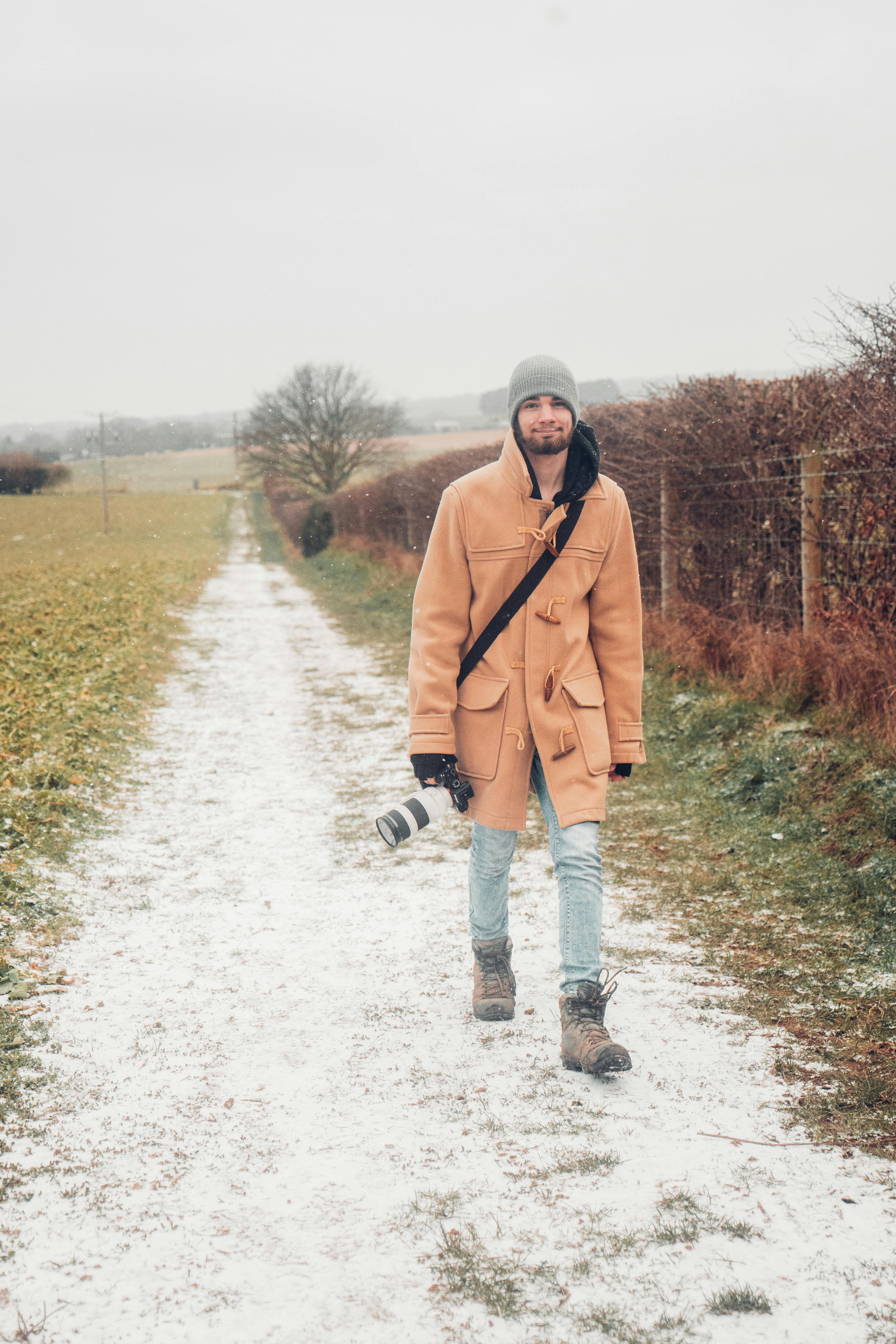 Man in Brown Coat Walking on Snowy Road · Free Stock Photo