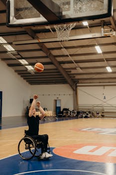 A wheelchair basketball player focuses intently as he shoots towards the hoop inside a sports hall.