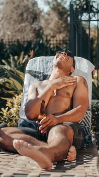 Man lounging on a sun lounger with a beer, enjoying a sunny summer day outdoors.