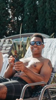 Smiling man enjoying a sunny day by the pool with a drink in hand, epitome of summer leisure.