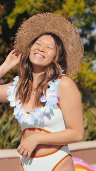 Woman wearing a bikini and sun hat, smiling joyfully at a summer pool party.