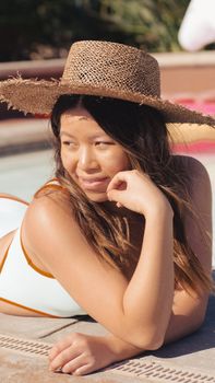 Woman in a straw hat and swimsuit enjoying a sunny day by the pool, epitomizing summer relaxation.