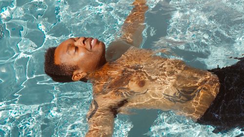 Free A man floats peacefully in a sunlit swimming pool, enjoying a relaxing summer day. Stock Photo