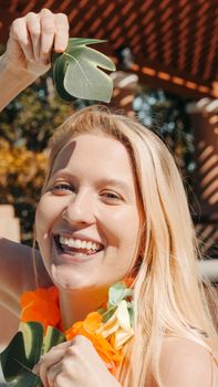 Joyful woman with a lei and leaf, embracing the summer sun with a bright smile.