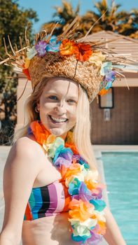 Woman enjoying a vibrant and fun poolside party with colorful leis and straw hat.