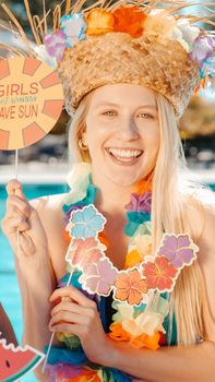 A smiling woman in a colorful headdress enjoying a fun poolside party wearing a floral necklace and hat.