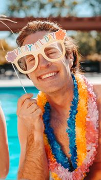 Smiling man with 'Vacay All Day' glasses at a vibrant summer pool party.