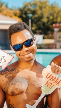 A cheerful man with sunglasses holding playful signs at a vibrant summer pool party.