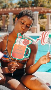 A joyful woman enjoying a poolside party, holding tropical-themed props and wearing a colorful bikini.