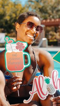 A joyful woman at a pool party holding colorful signs under the sun, embodying summer fun.