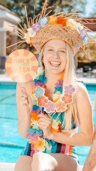 Smiling woman with straw hat and lei relaxing at a vibrant poolside party.