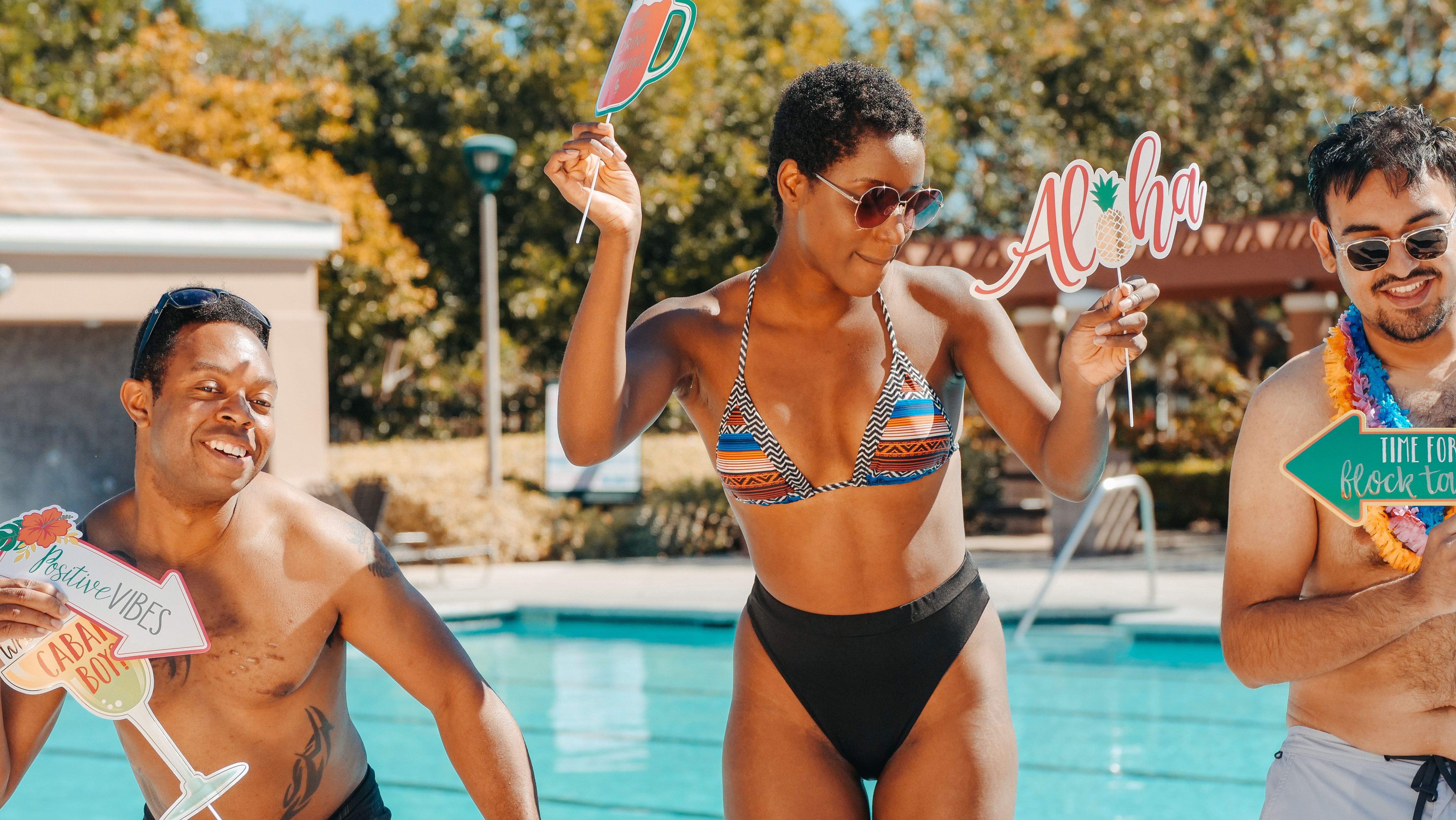 Group of friends celebrating at a pool party with fun props, smiles and sunshine in summer.