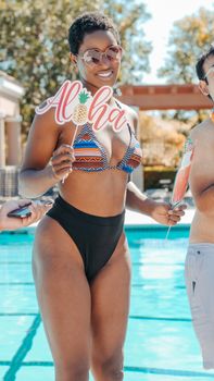 Confident woman in colorful bikini holding aloha sign by a pool, enjoying summer vibes.