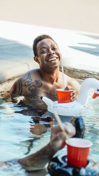 Smiling man enjoying a summer pool party with drinks and friends, relaxing in the water.