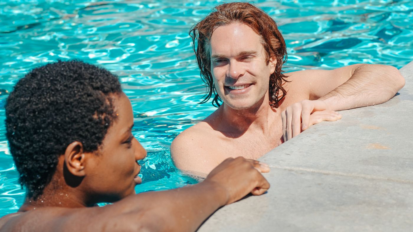 Two men relaxing and talking together by a pool, at ease