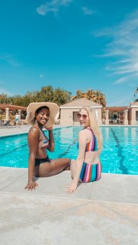 Two women enjoying a sunny day by the pool, smiling and relaxing together.
