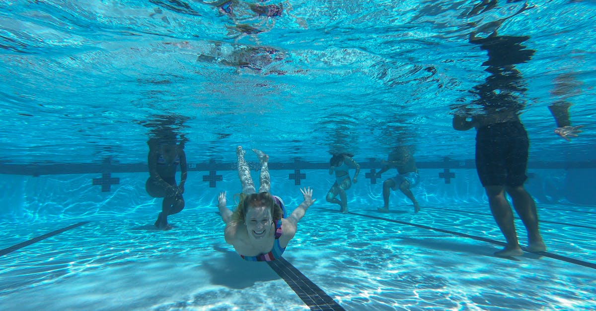 Young woman enjoys swimming underwater in a clear pool, surrounded by friends on a sunny day.
