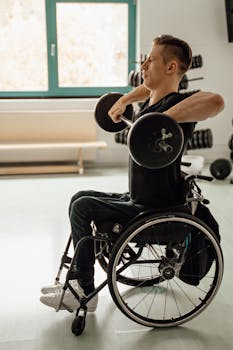 A man in a wheelchair lifts weights in a gym, demonstrating strength and determination.