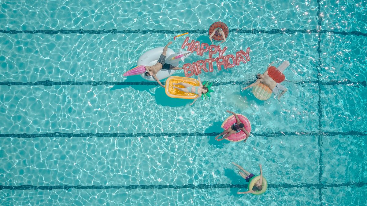 Top view of friends enjoying a summer pool party with floats and 'Happy Birthday' balloons. Stock Photo.