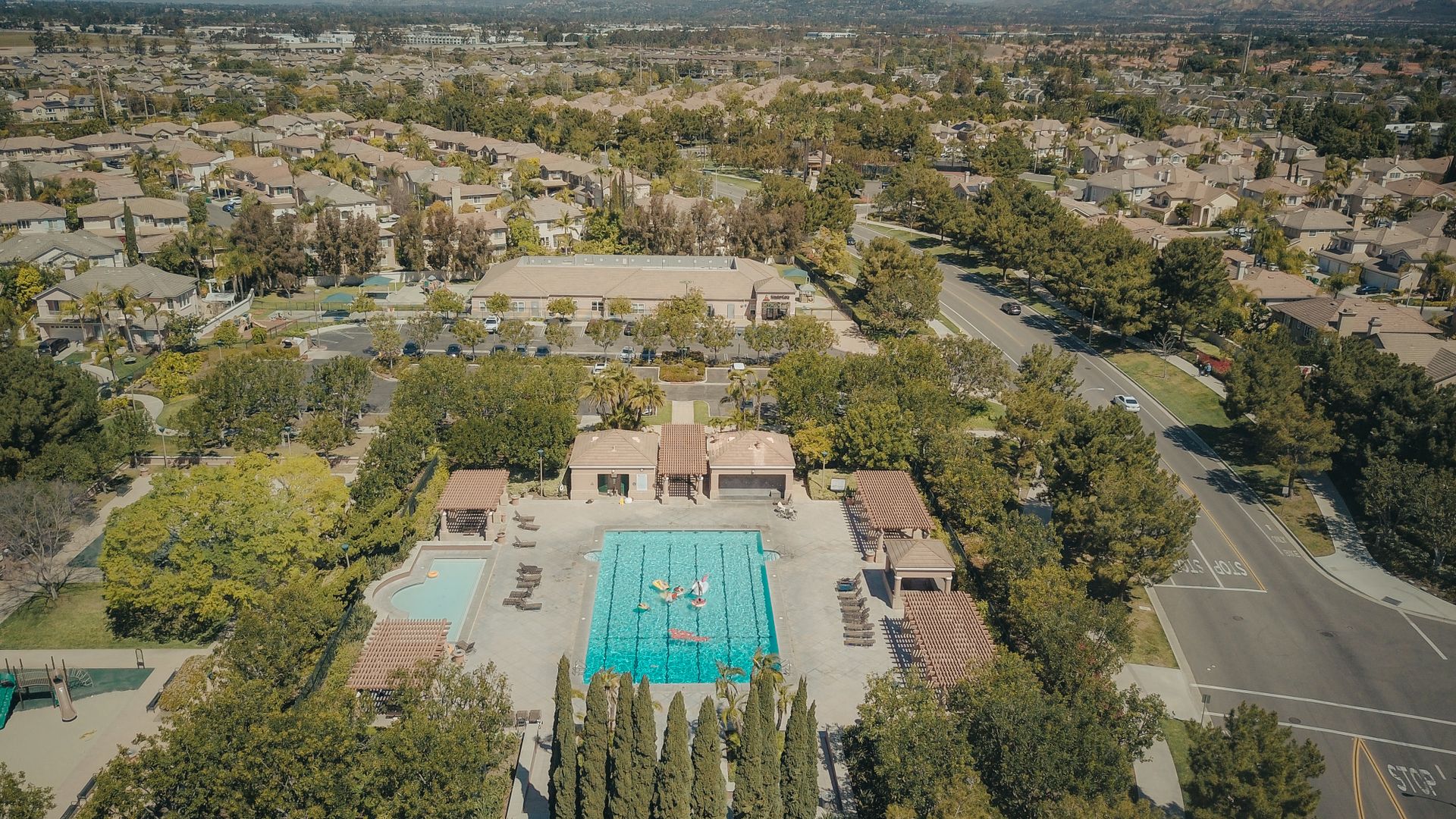 Aerial view of a residential neighborhood with a busy swimming pool and surrounding greenery.