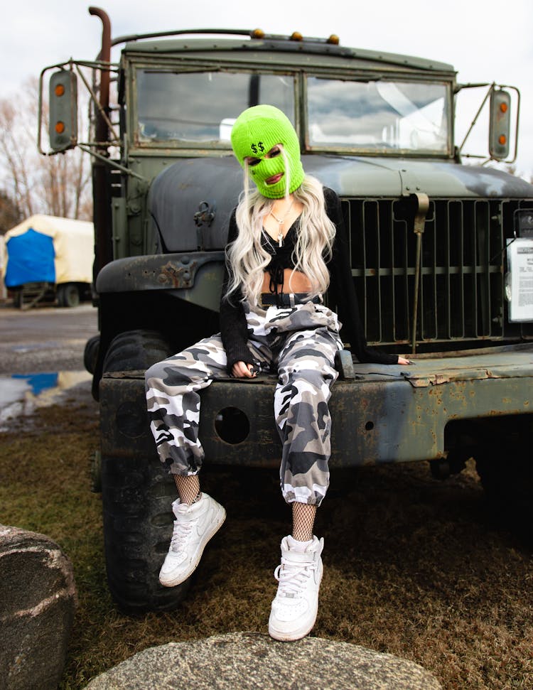 Woman In Green Ski Mask Sitting On Old Truck  Bumper