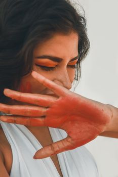 A thoughtful portrait of a woman with red paint on her hand, eyes closed, and a serene expression.