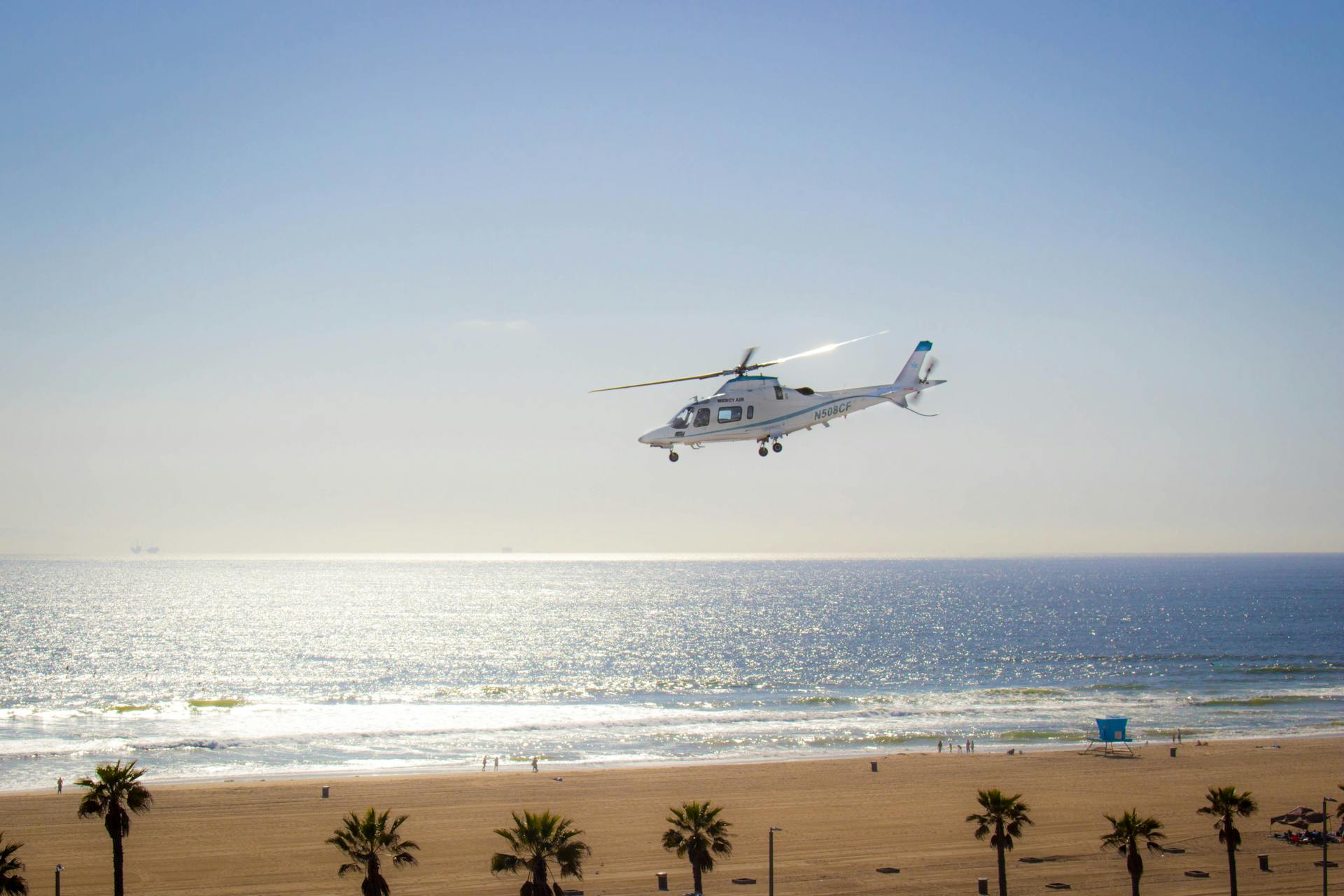 A helicopter flying over the sparkling waters of Huntington Beach on a clear day.