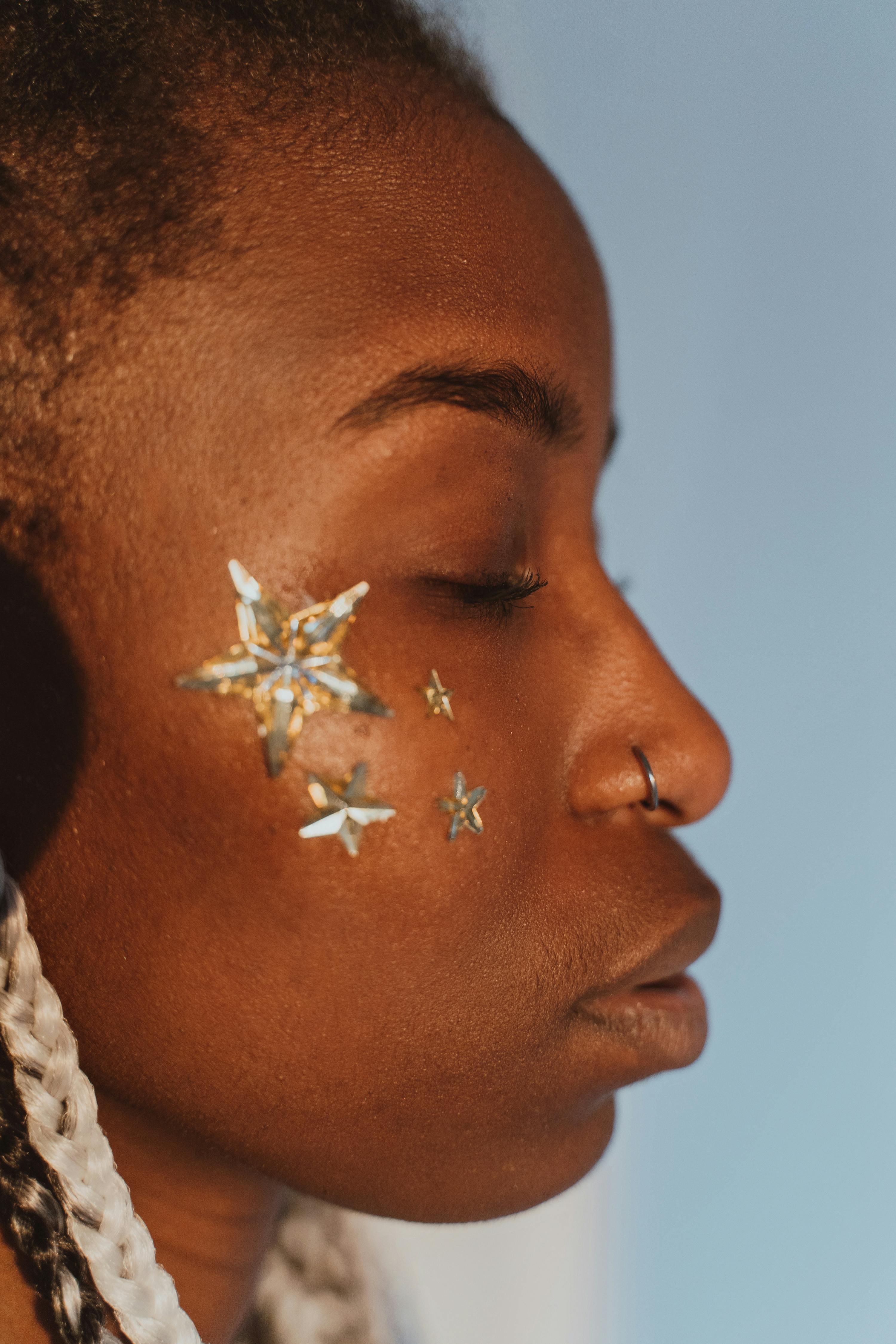 Artistic close-up portrait of a woman with star face stickers and a nose piercing.