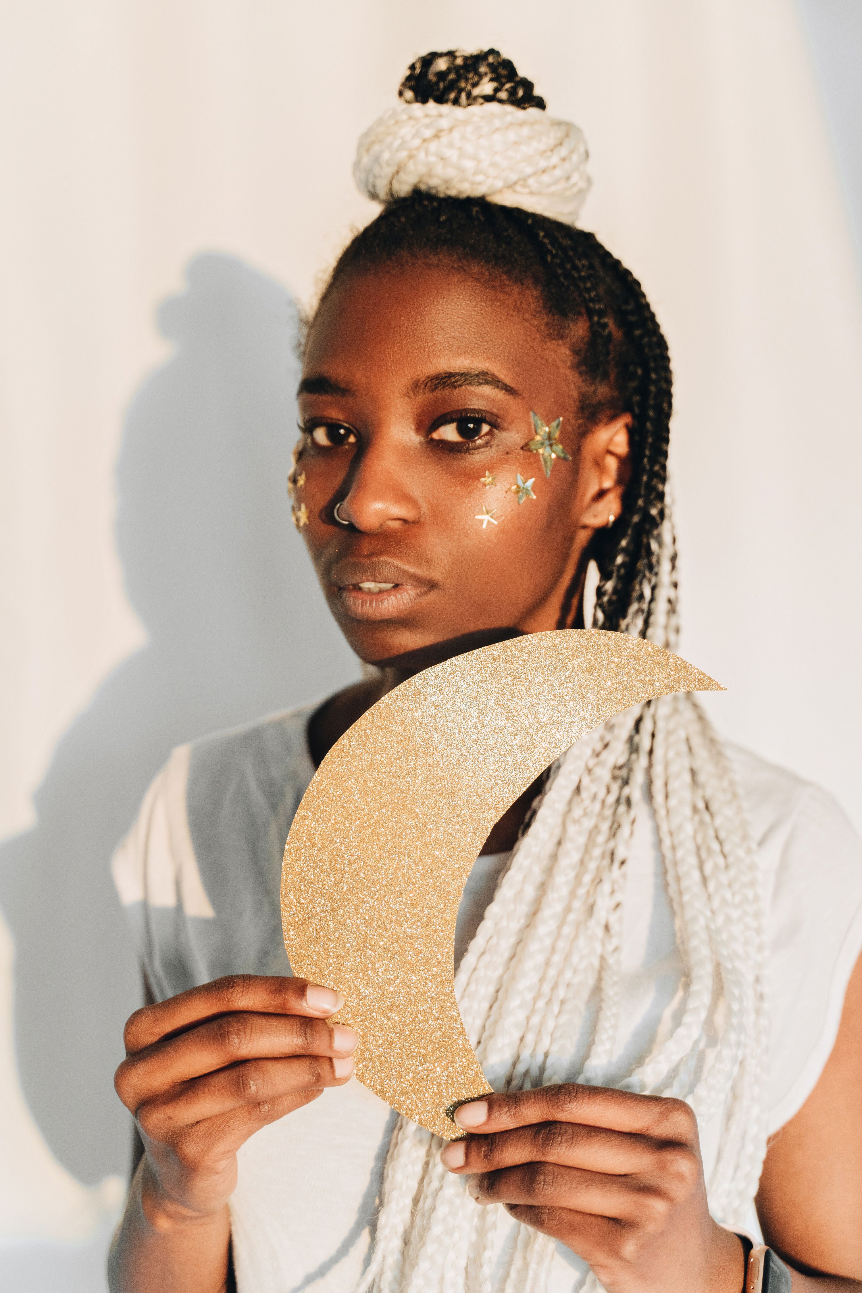 Stylish portrait of woman holding a glittery crescent moon with star decorations on her face.
