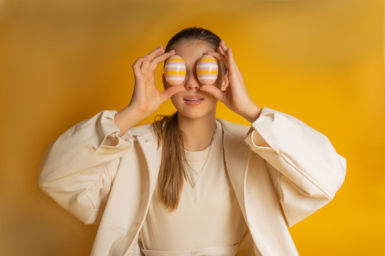 a young woman playfully holds painted easter eggs over her eyes agains