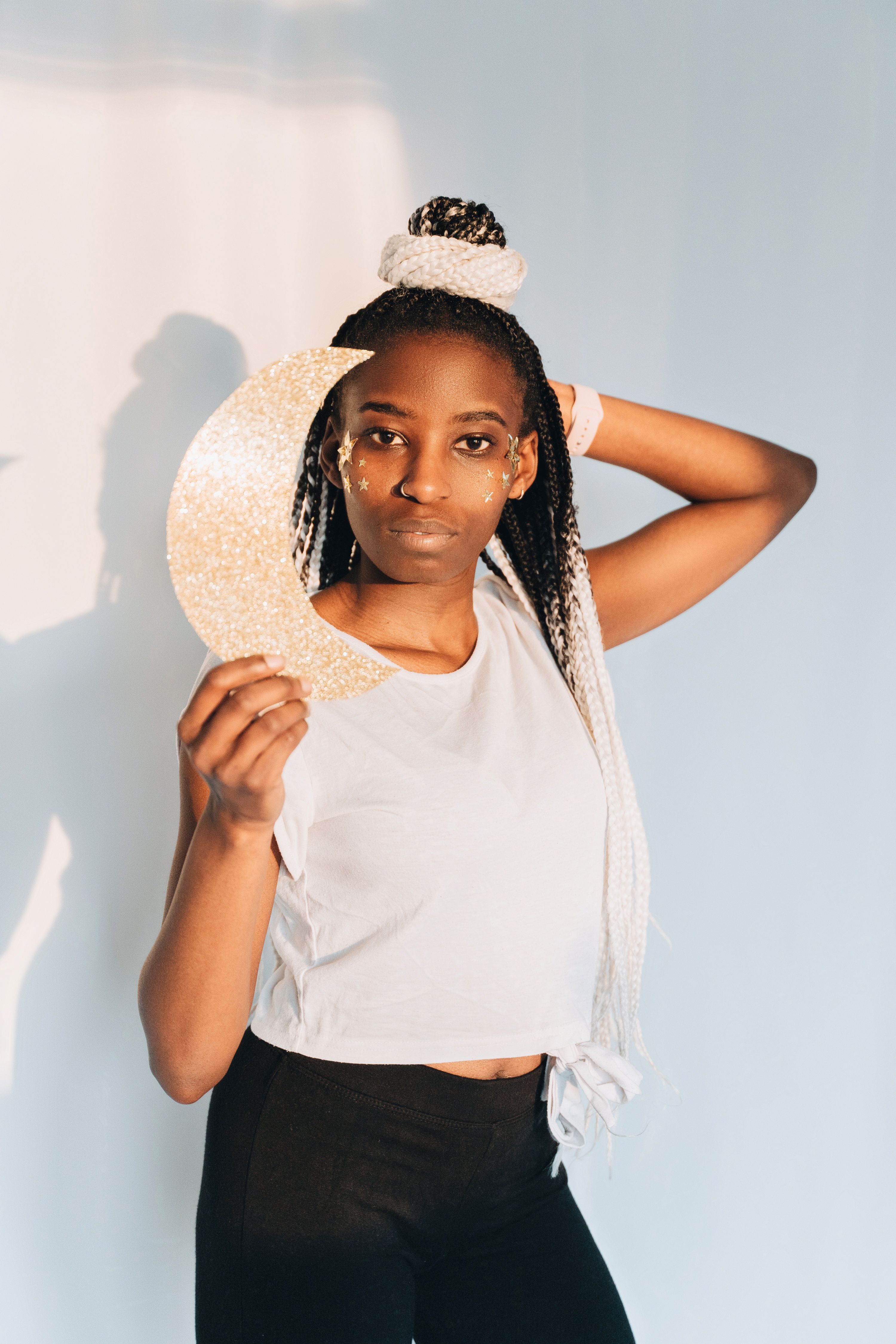 Beautiful African woman poses with a glittery crescent moon against a pastel background, showcasing modern fashion.