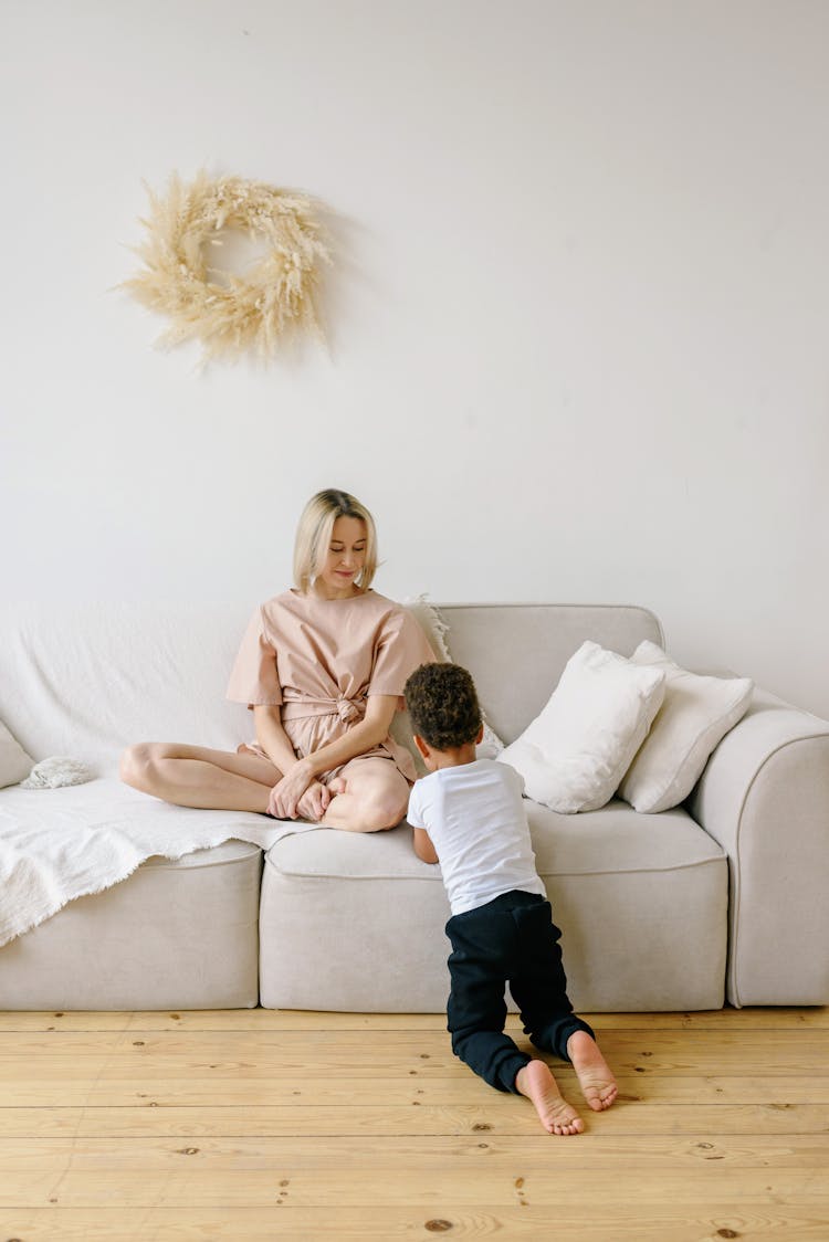 Woman Sitting On Couch Looking At Kid Kneeling On Floor